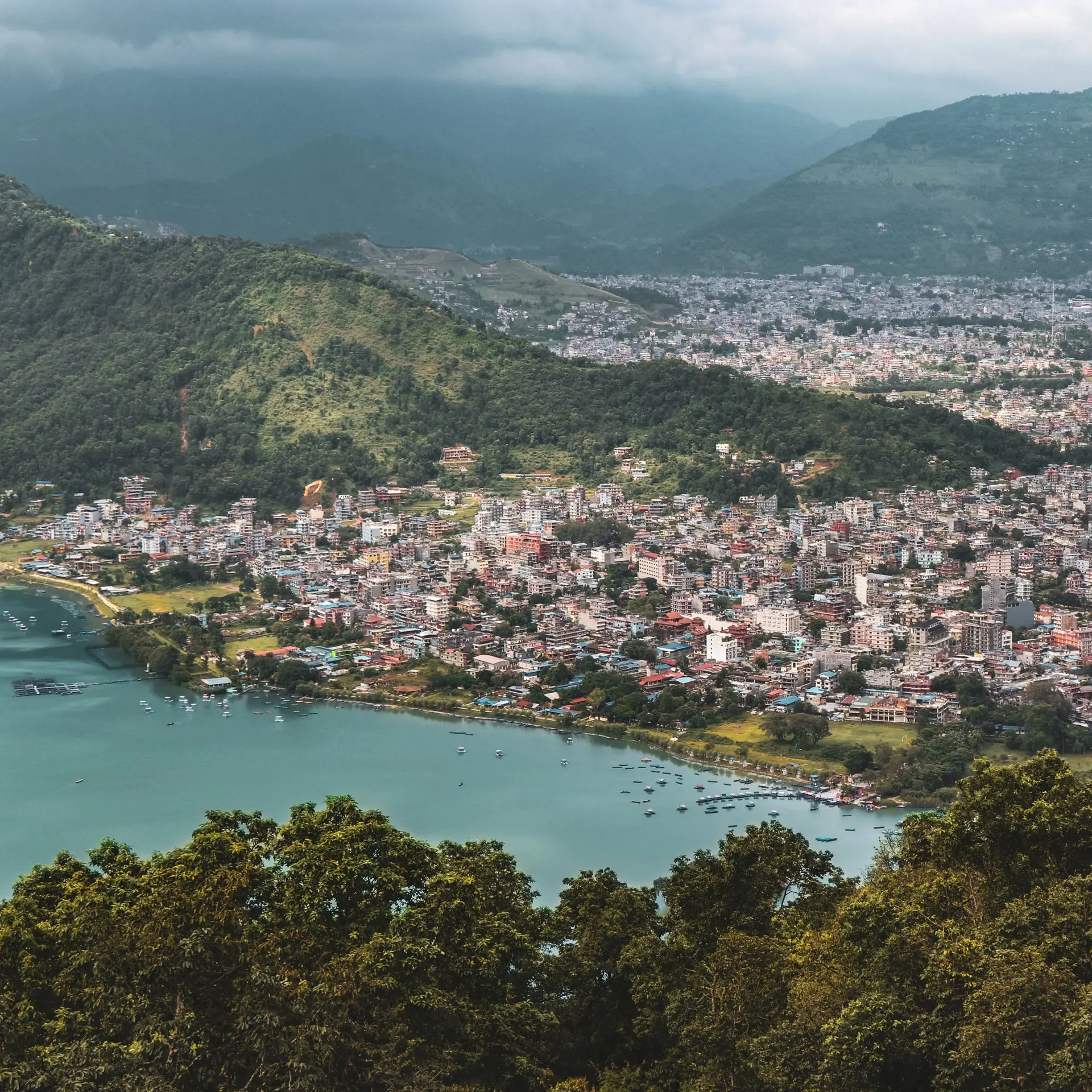 Aerial view of Pokhara’s lakeside buildings, boats and surrounding green hills in Nepal.